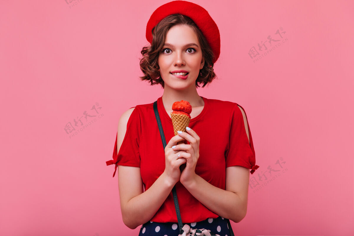 女人穿着红色上衣的迷人白人女孩正在吃冰淇淋幽默的法国女模特拿着甜点站着贝雷帽时尚甜点