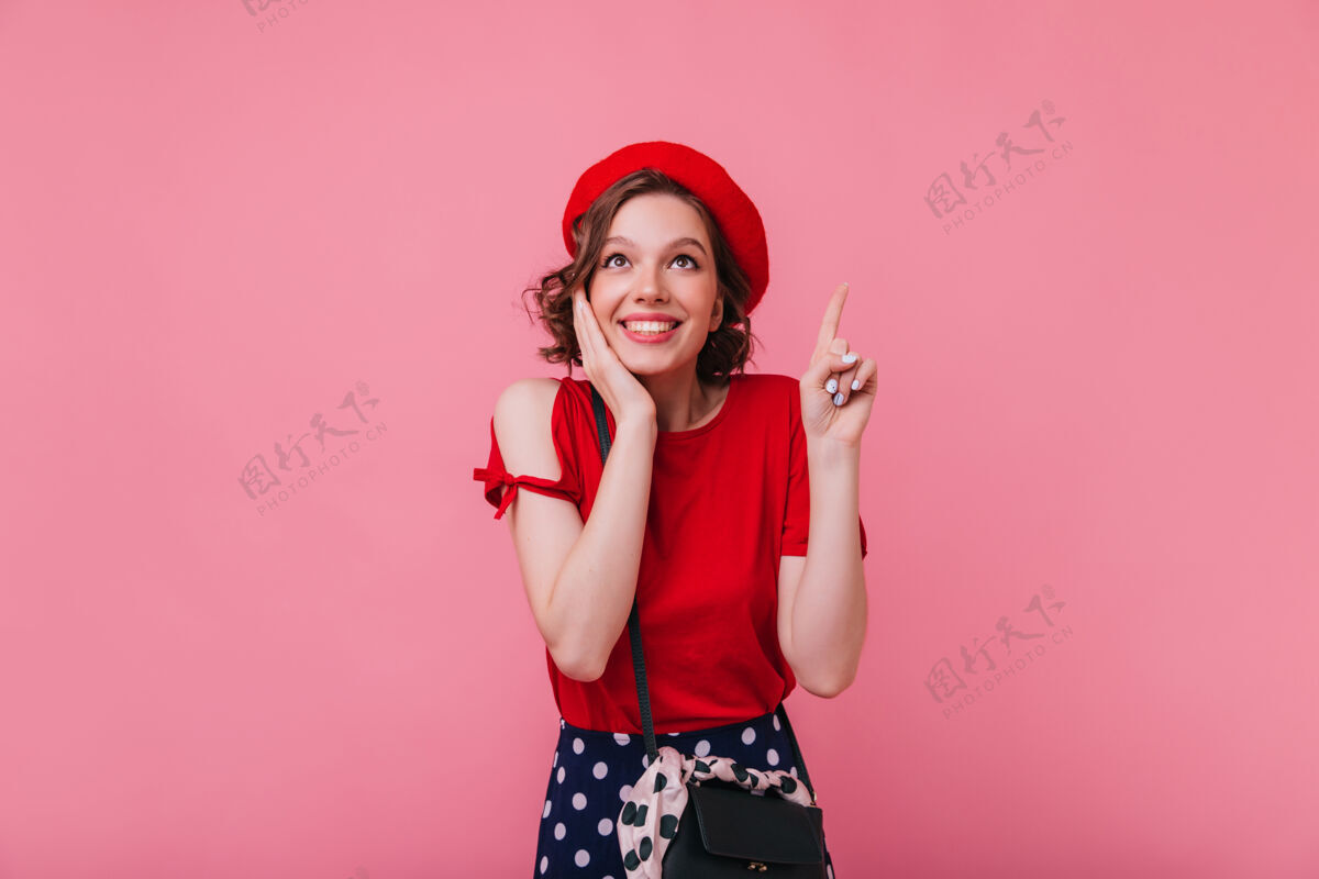 表情美丽的法国女孩 波浪形的发型 带着惊奇的微笑摆出姿势优雅的白色女人戴着红色贝雷帽的室内照片漂亮粉色可爱