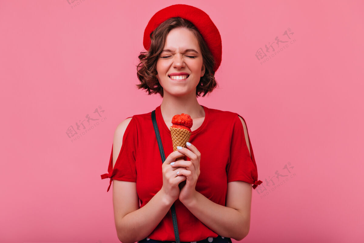 室内可爱的短发女孩愉快地吃着冰激凌身着红色衣服的快乐白人女士站在那里的室内照片享受快乐年轻