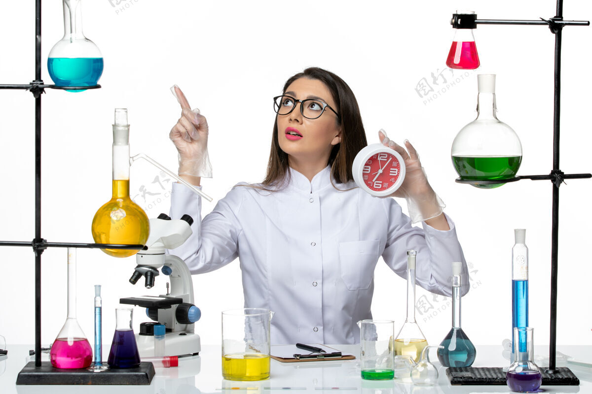 时钟前视图穿着白色医疗服的女化学家手持红色时钟 背景是白色的科学病毒实验室病毒-大流行病毒工作持有