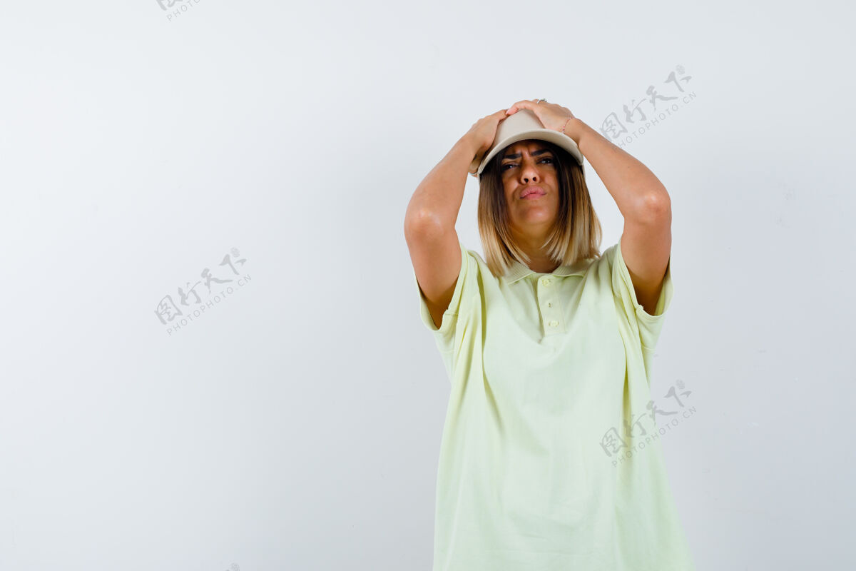 模型穿着t恤 戴着帽子的年轻女士 手举在头上 看起来健忘 正面视图手成人皮肤护理