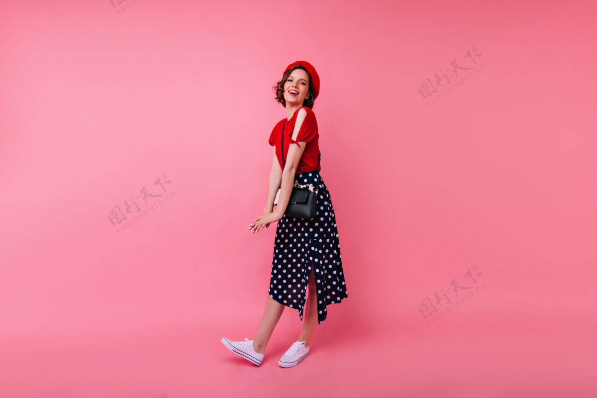 女性穿着白色运动鞋的快乐的欧洲女人的全长肖像穿着法国红色贝雷帽的快乐的女孩漂亮成人模特