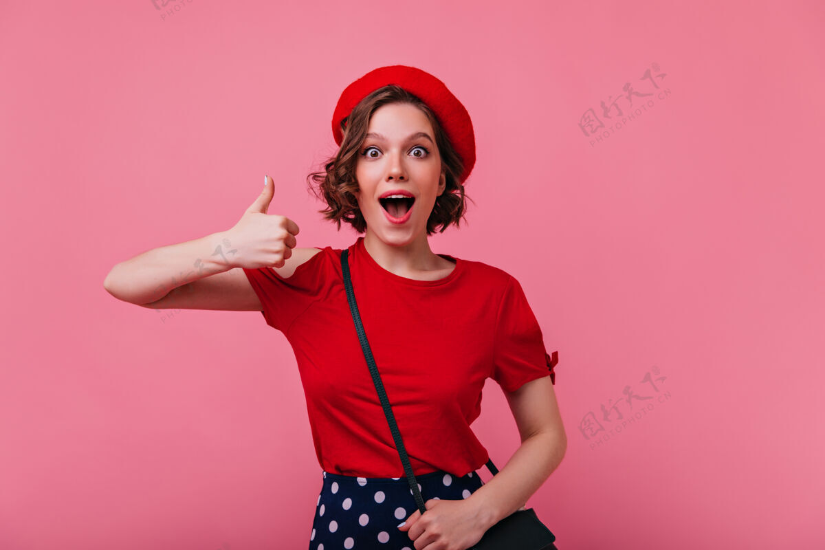 人迷人的兴奋的女人摆出拇指向上的姿势穿着时髦的红色贝雷帽的快乐的法国女孩的室内肖像时尚人物优雅
