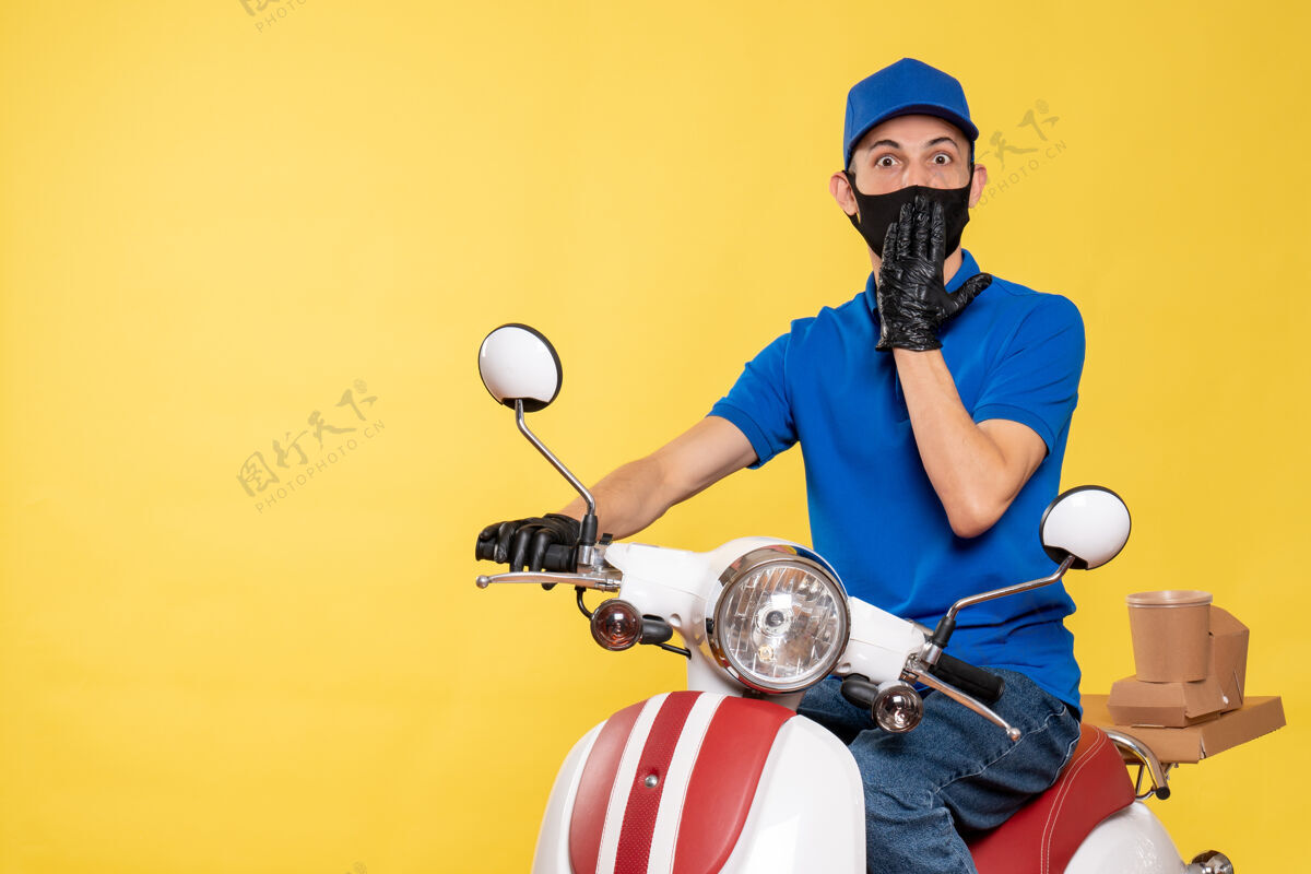 摩托车正面图：身穿蓝色制服 戴着黄色工作面罩的男性快递员-快递大流行自行车作业病毒高尔夫球员人