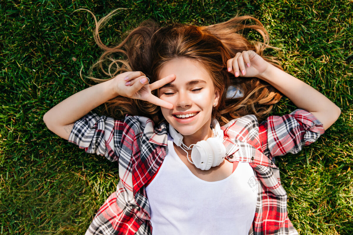 无忧无虑悠闲的白人女孩躺在草坪上 打着和平的牌子头顶上拍着一个相当幽默的女人微笑情感年轻