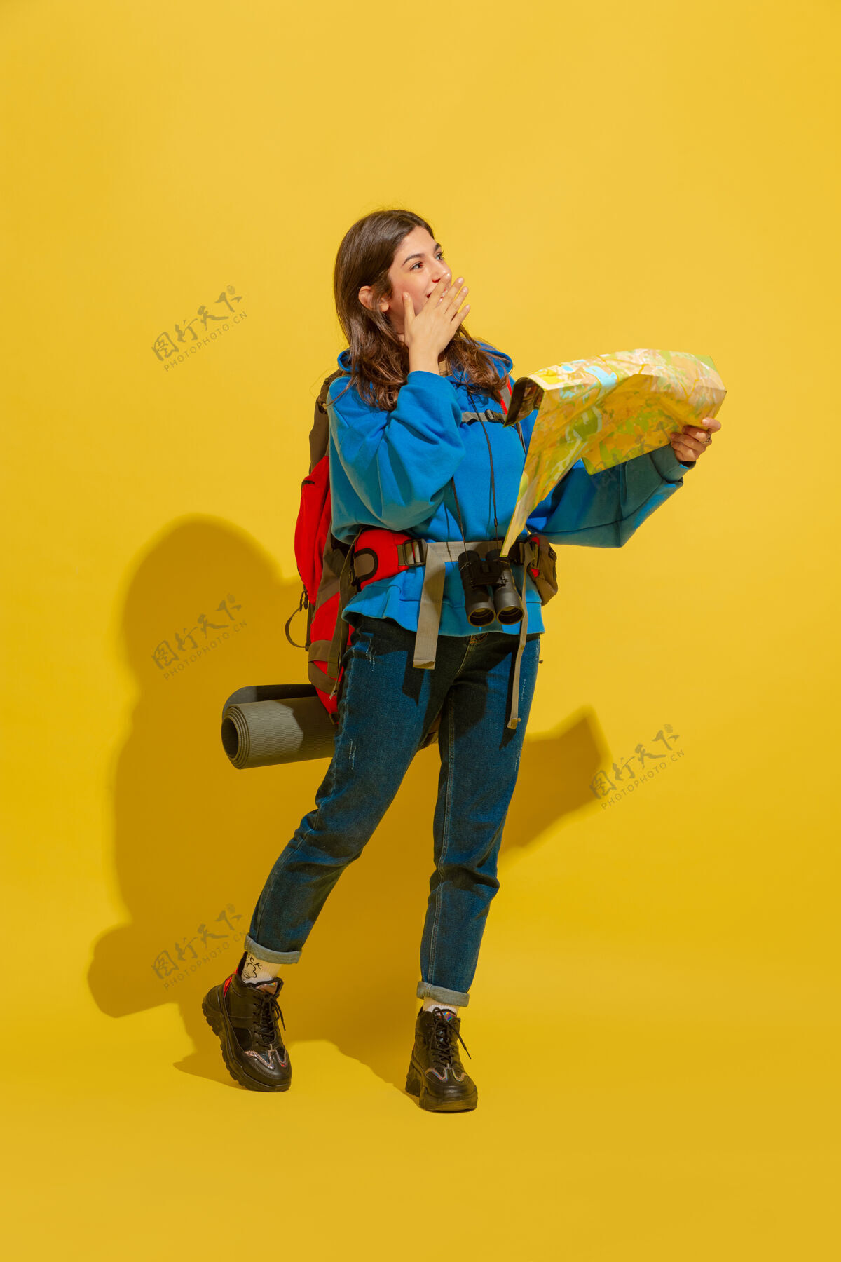 女孩微笑着 寻找出路一个快乐的年轻高加索旅游女孩的肖像 带着包和望远镜 隔离在黄色的工作室背景上衣服度假黄色