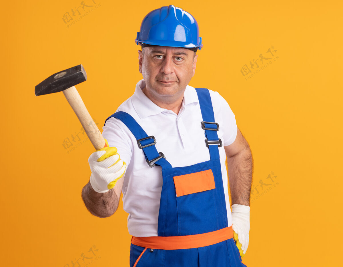人高兴的白人成年建筑工人穿着制服 戴着防护手套 手里拿着橘子锤制服锤子人