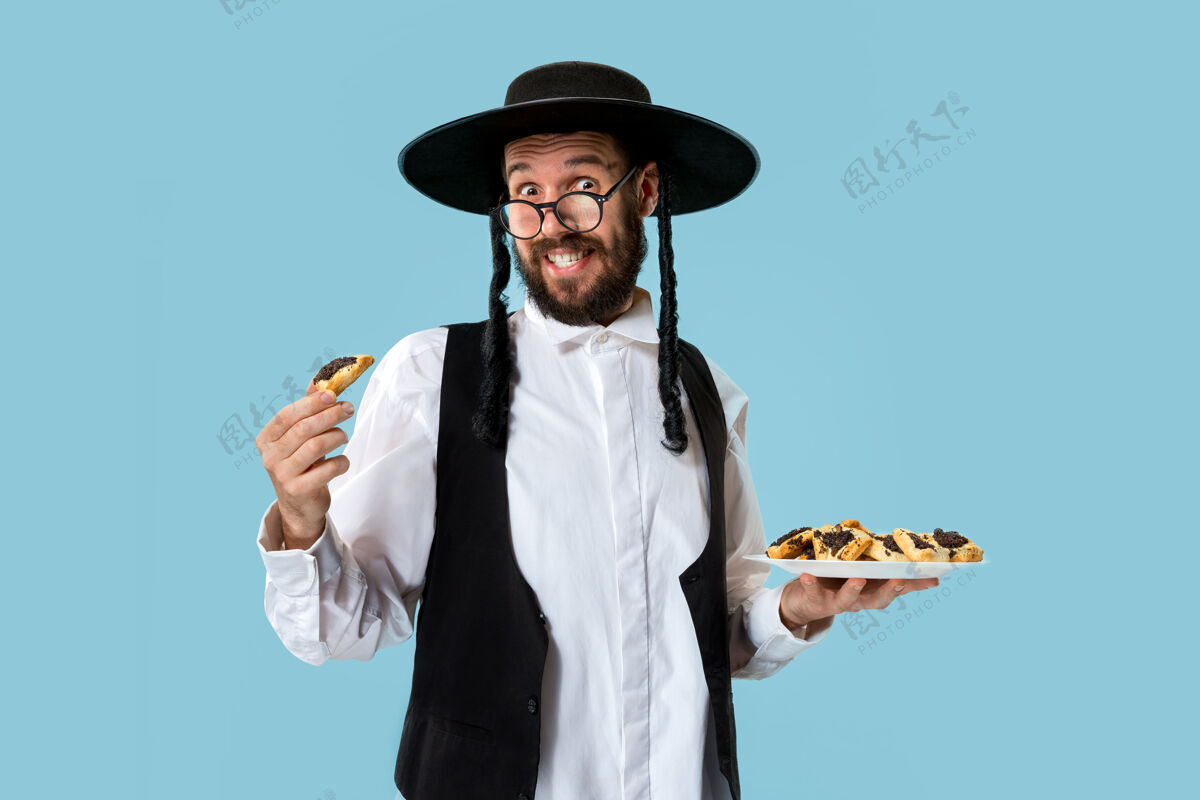 文化这位年轻的东正教犹太男子戴着黑帽子 在犹太普瑞姆节上吃哈曼塔森饼干曲奇食物犹太教