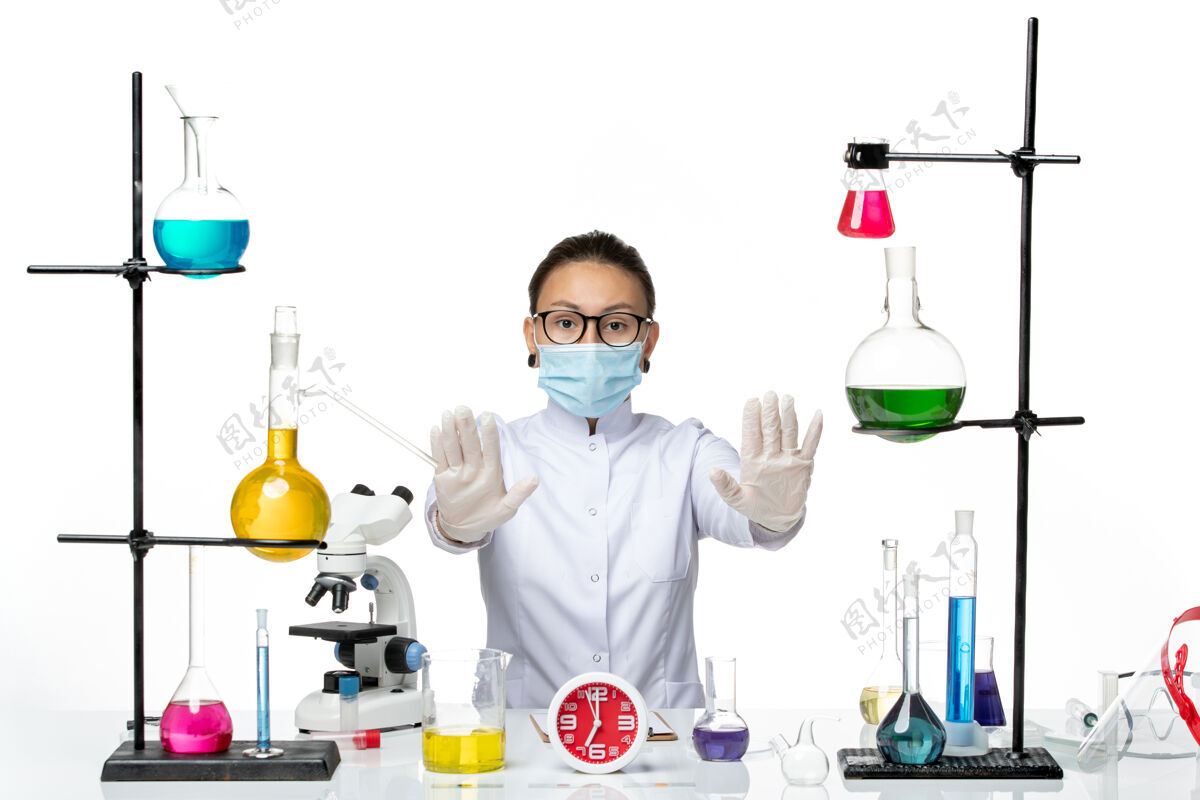 实验室前视图穿着医疗服的女化学家戴着面罩坐在白色背景上看化学家实验室病毒-飞溅飞溅医学解决方案