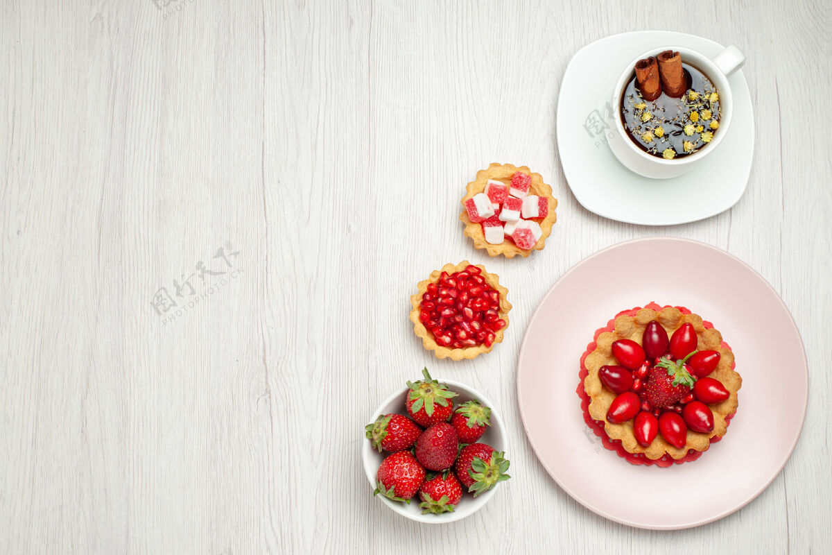 草莓俯瞰白色书桌上的奶油蛋糕和一杯茶多汁小奶油蛋糕浆果