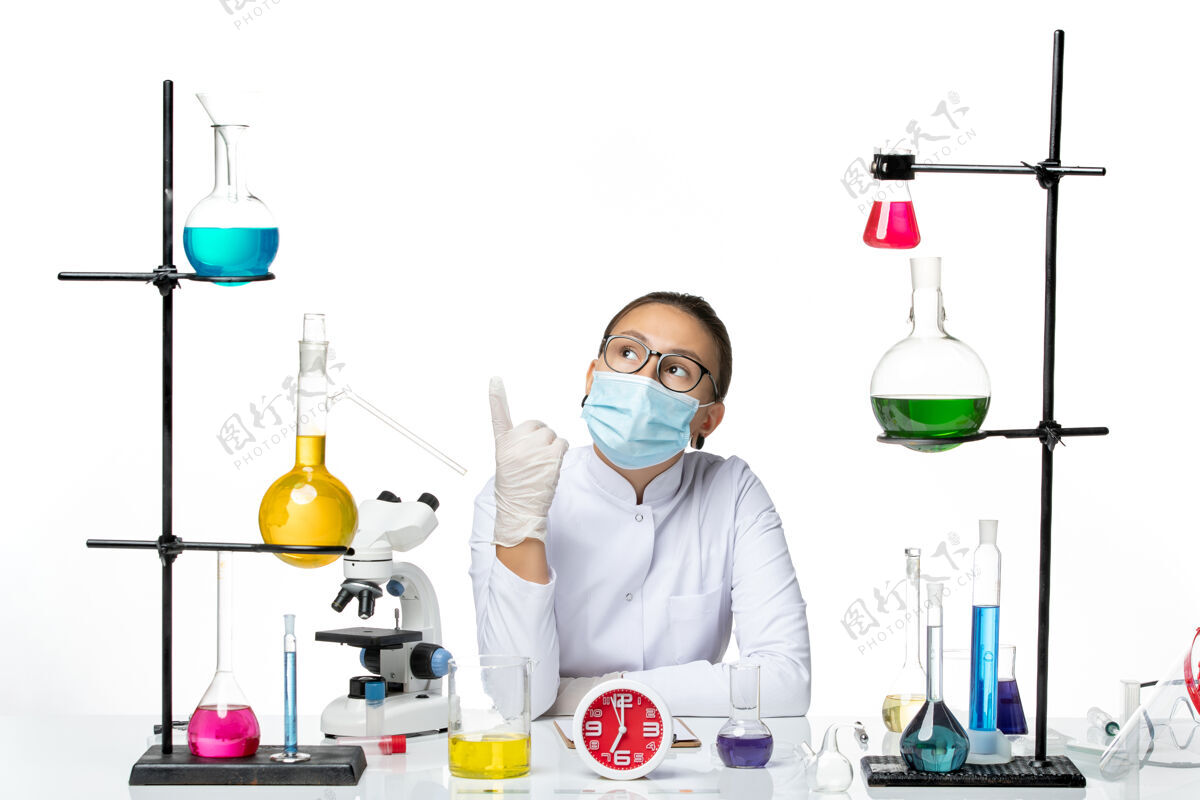 实验室前视图穿着白色医疗服的女化学家带着面罩坐在浅白背景上的溶液化学家实验室病毒-飞溅前面化学家医学