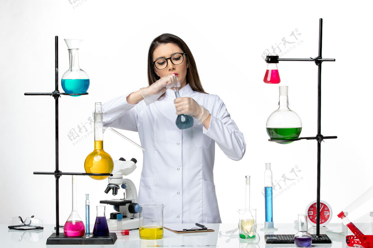 大流行正面图：穿着无菌医疗服的女化学家在白色背景病毒冠状病毒上用不同的溶液工作-大流行科学专业医学不同