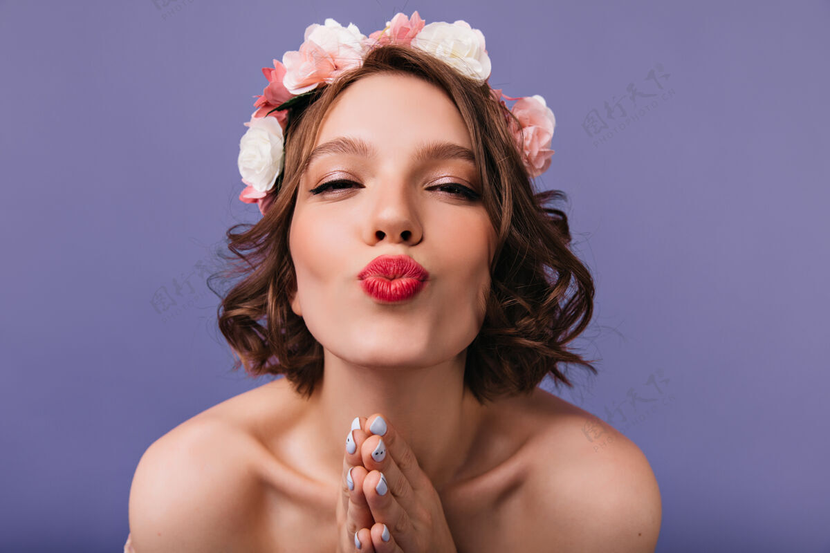 欧洲幸福的白色女孩的特写肖像 粉色的玫瑰在头发上迷人的女人戴着花环摆出亲吻的表情女士微笑紫色