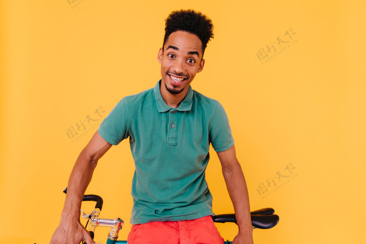 非洲一个穿着绿色t恤的骑车人带着惊讶的微笑摆出姿势坐在自行车旁边的一个惊讶的黑发男人的肖像黑色放松家伙