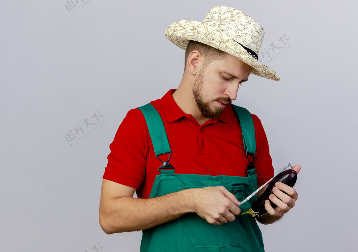 帅哥年轻英俊的斯拉夫园丁穿着制服 戴着帽子 手里拿着茄子 用卷尺量着它带子年轻人男人