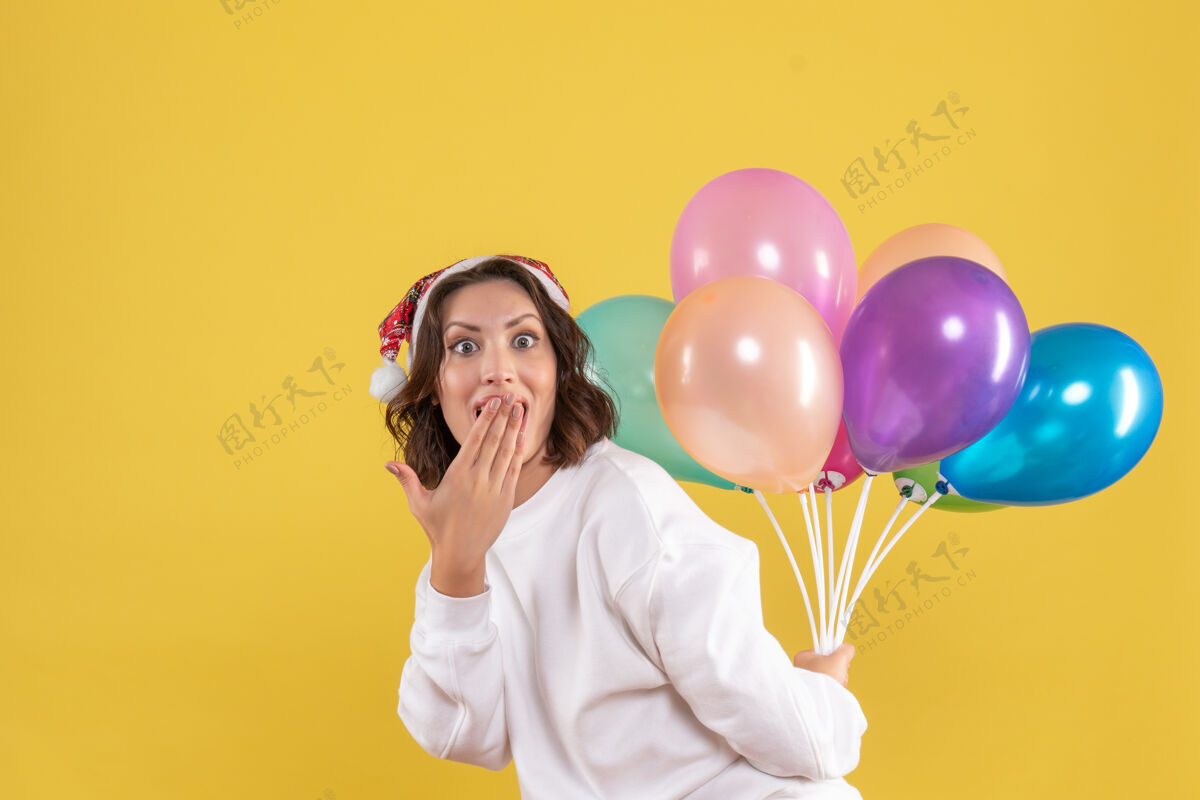 年轻女性正面图年轻女子藏着五颜六色的气球新年圣诞彩绘节日女子感慨圣诞节吹生日