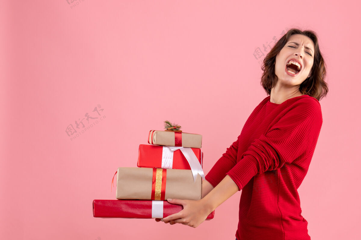 礼物正面图：年轻女性拿着圣诞礼物放在粉色书桌上圣诞假期感慨女人新年风景正面笔记本电脑