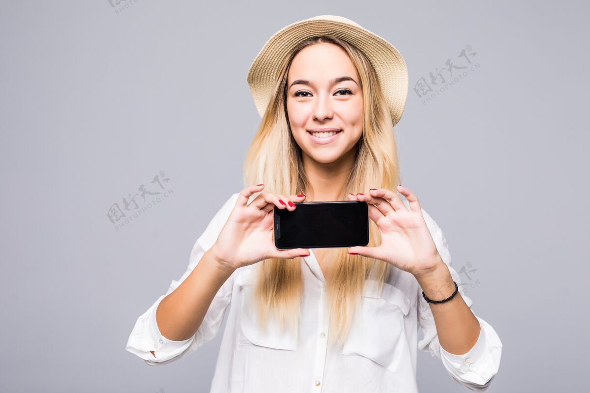 休闲穿着休闲服的快乐女人在灰色的墙上展示着空白的智能手机屏幕欢呼显示女性