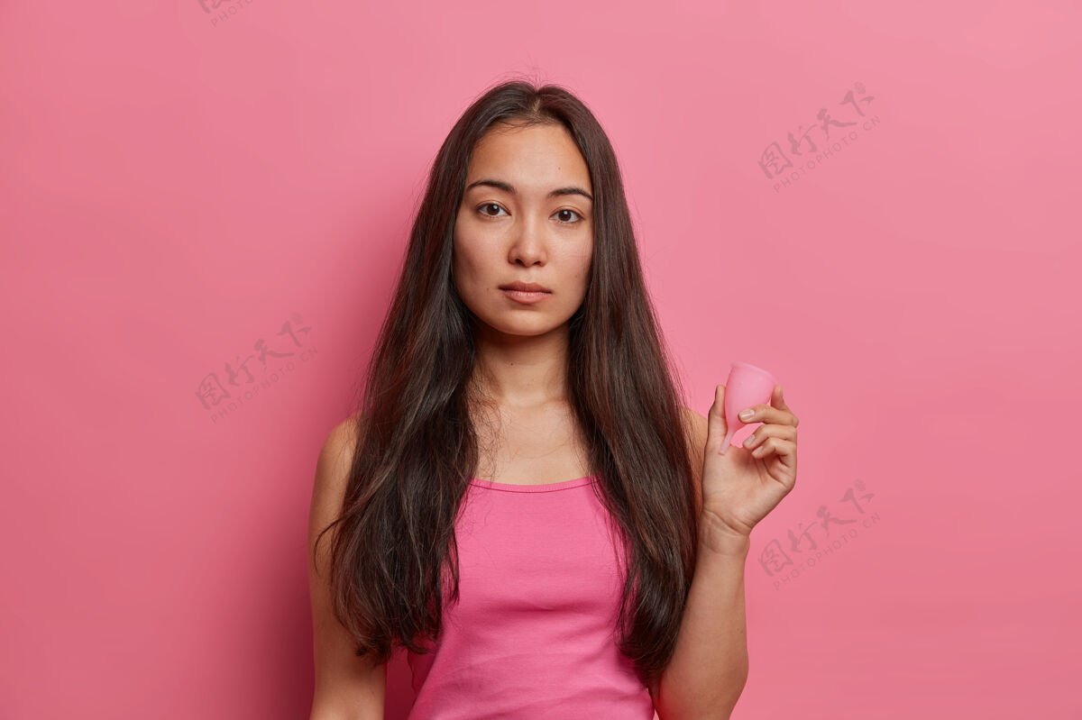 亲密月经保护 妇科和女性卫生观念严肃的深色人种妇女拿着月经杯 在血液周期使用零废物吸收剂产品 隔离在粉红色的墙壁上女性液体周期