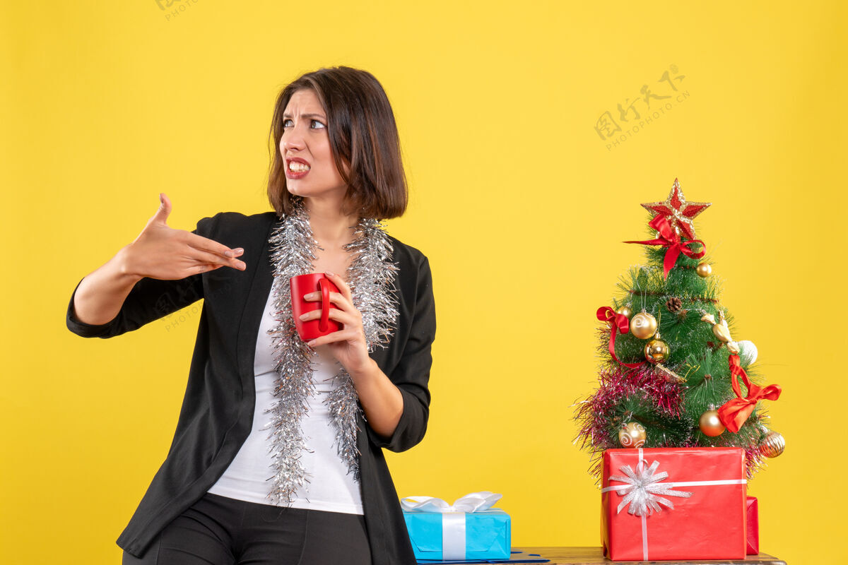 漂亮圣诞节的心情与情感美丽的女士站在办公室里 拿着红色的杯子在黄色的办公室性感快乐人