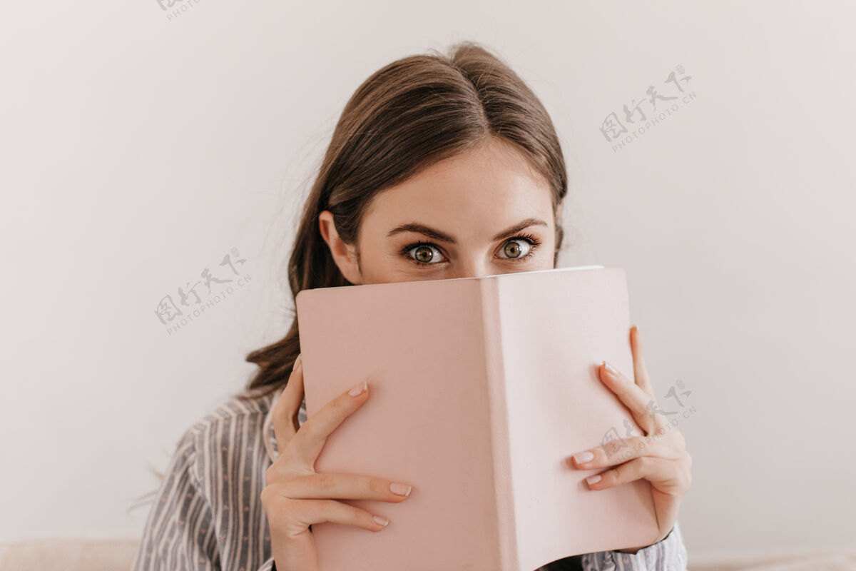 放松穿着条纹睡衣的绿眼睛女人看着前面 用笔记本遮住脸房间独自人