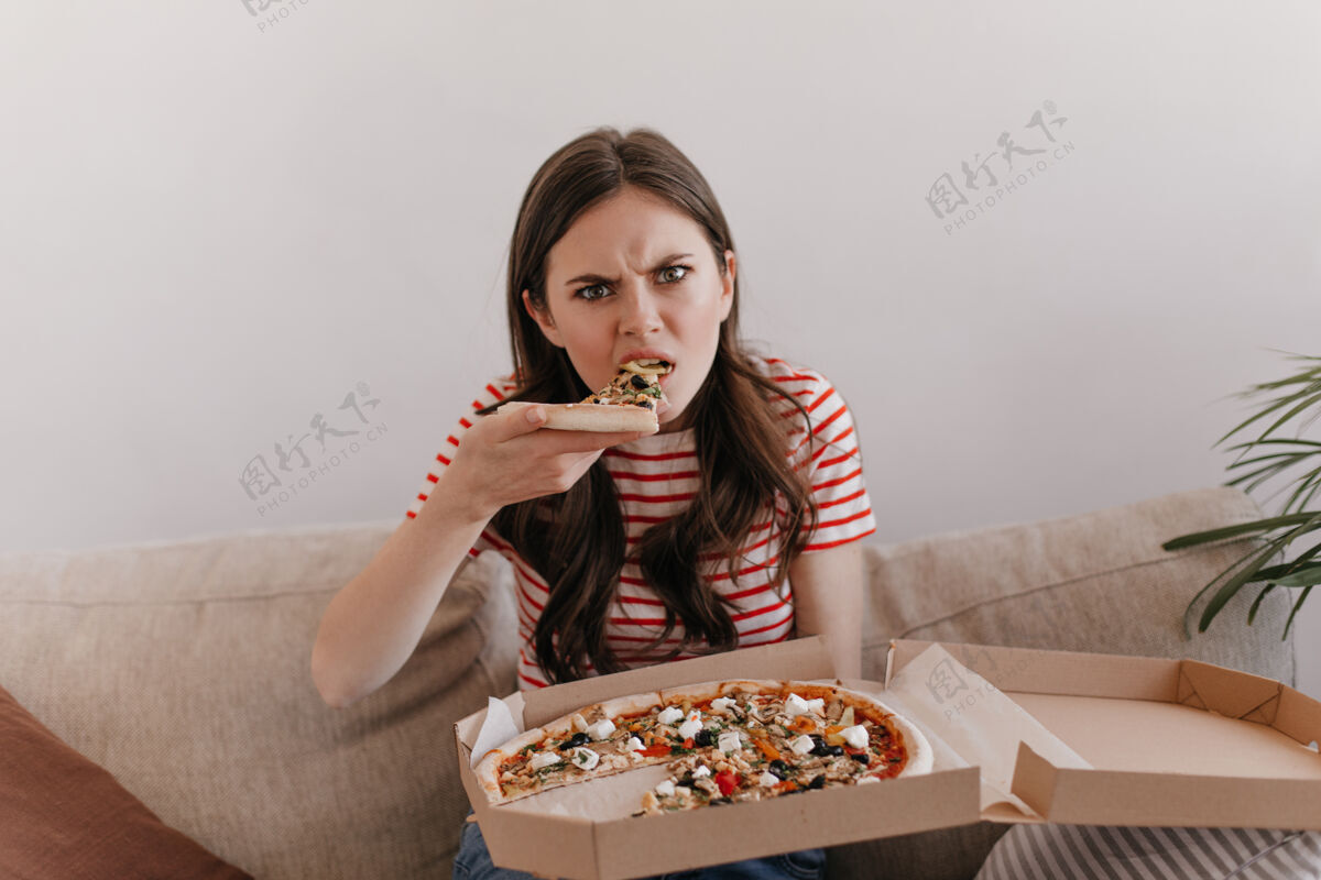 美味一个穿着条纹衬衫 饥肠辘辘的女人咬着新鲜的比萨饼肖像公寓休闲