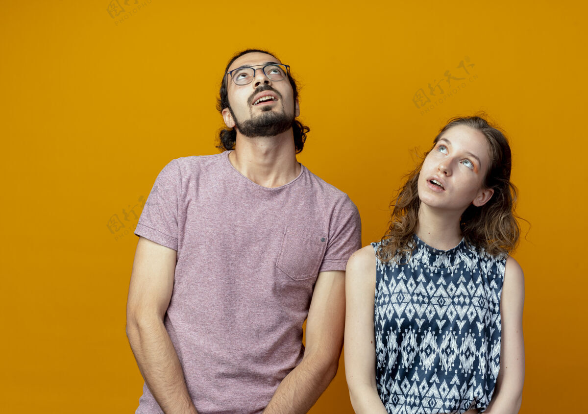 情侣年轻漂亮的夫妇站在橙色的背景下 困惑地抬起头来年轻站着拼图