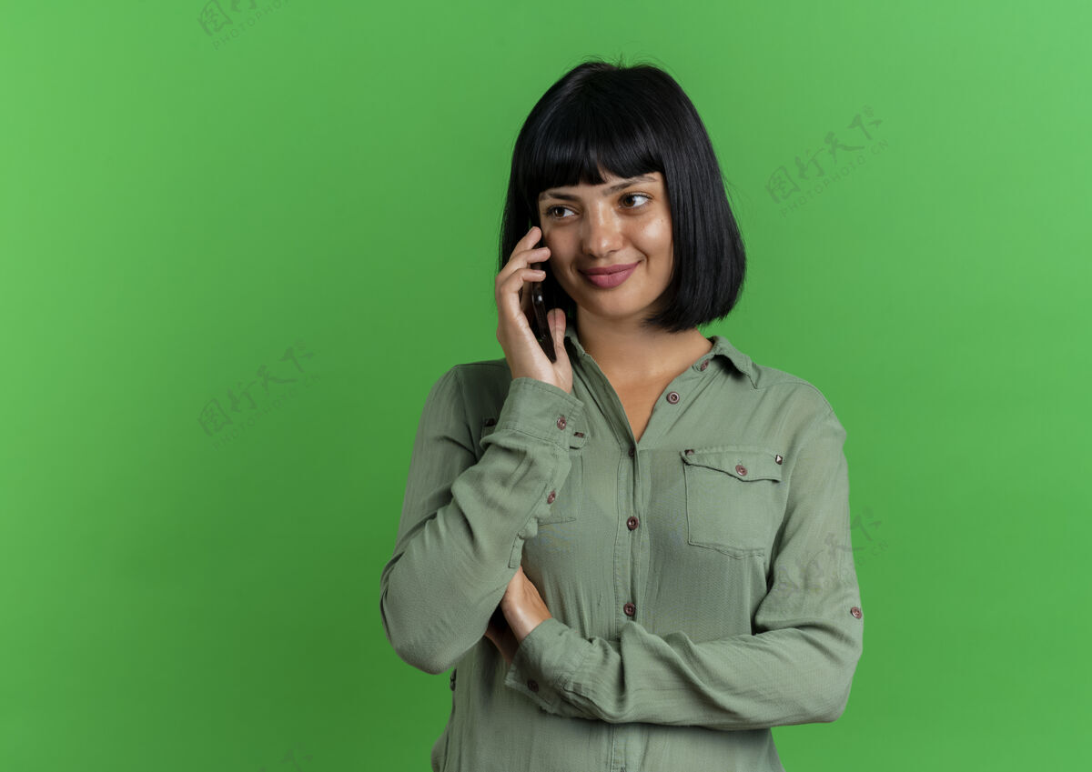 年轻高兴的年轻黑发高加索女孩在电话里交谈看着绿色背景和复印空间上孤立的一面女孩壁板黑发