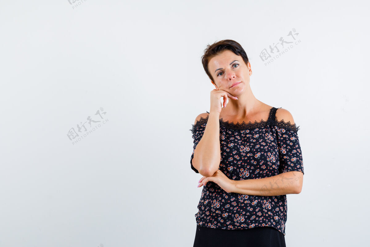 女性穿着花衬衫和黑色裙子的成熟女人 手托下巴 一只手放在胳膊肘下 神情沉思 俯视前方年龄优雅商务