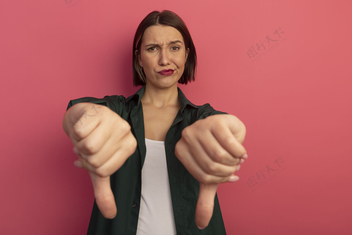 女人一个未被释放的漂亮女人竖起大拇指 两只手被隔离在粉红色的墙上向下站着人
