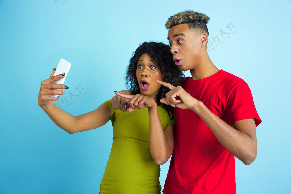金融一起自拍或视频录影带年轻情绪化的非洲裔男女 穿着蓝色背景的彩色衣服美丽的情侣人类情感的概念 面部表情 关系 广告朋友一起广告
