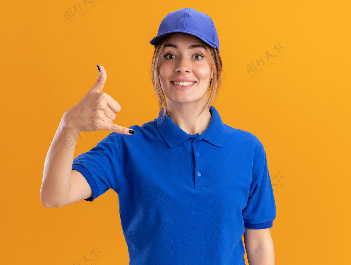衣服微笑着的年轻漂亮的女送货员 穿着制服 在橘色的墙上做着一个松散的姿势脸手势公民