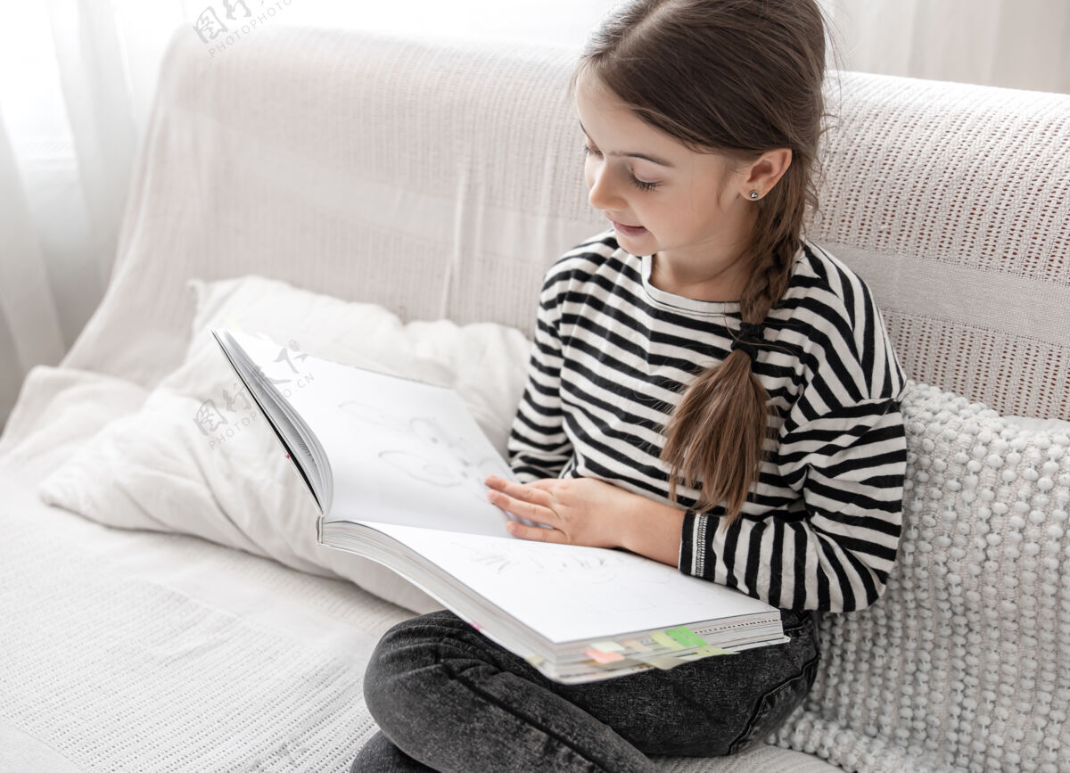 阅读一个可爱的小女孩坐在家里的沙发上 兴致勃勃地翻阅着一本书女学生房子发展