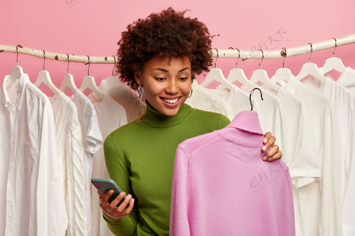 选择正黑女人选毛衣买 用紫色高领毛衣 手机在另一只手里拿衣架服装请手机