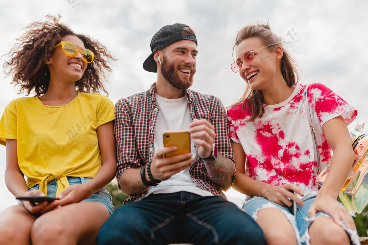 青春快乐的年轻朋友坐在公园里用智能手机微笑公司眼镜情感享受