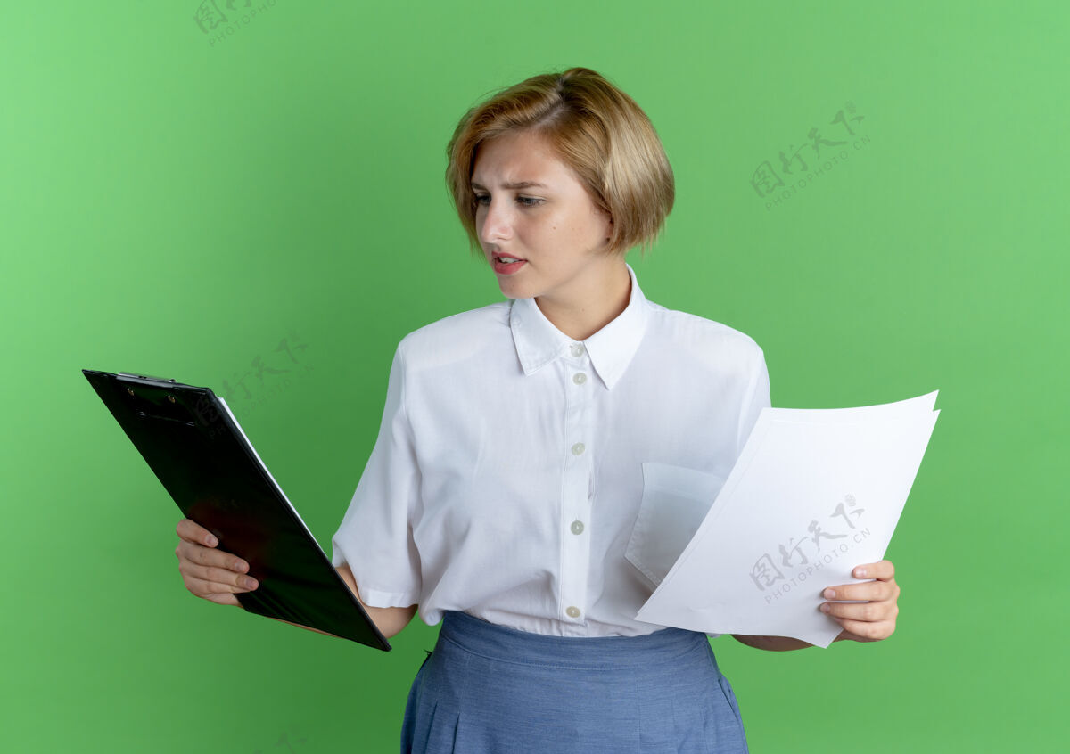 持有年轻困惑的金发俄罗斯女孩拿着纸页 看着剪贴板上的绿色背景与复制空间隔离年轻困惑床单