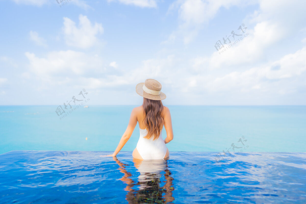 周末肖像美丽的亚洲年轻女子放松微笑休闲在户外游泳池周围与大海在旅游度假热带休闲泳装