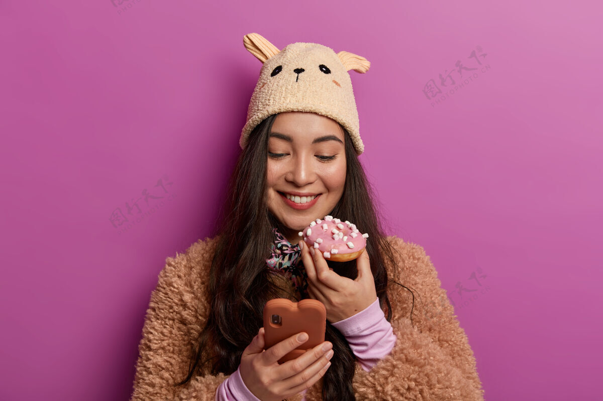 美味食物和卡路里的概念快乐的千禧一代女孩胃口大吃甜甜圈 通过手机在线聊天 喜欢吃甜点女士味道亚洲