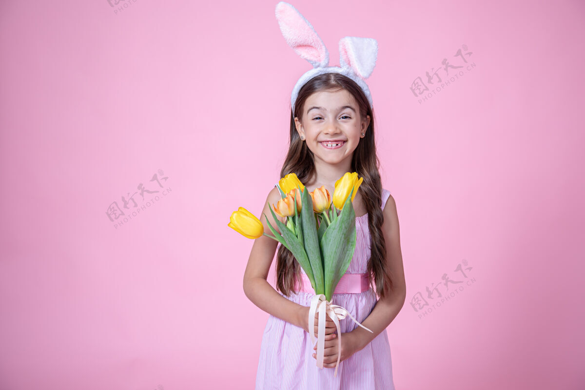 孩子带着复活节兔子耳朵的快乐小女孩微笑着 手里拿着一束郁金香放在粉红色的墙上春天花郁金香