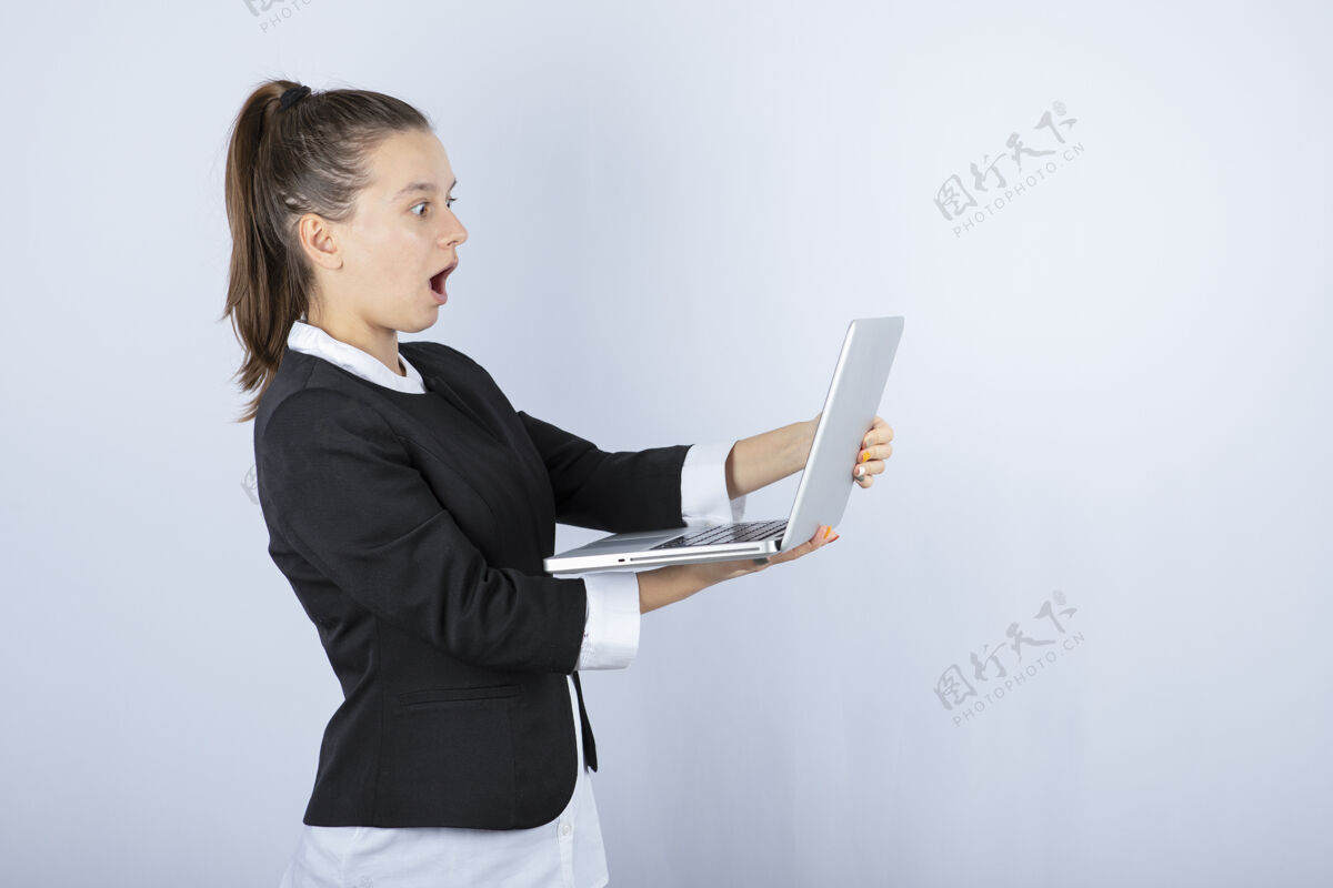 站立年轻女子在白墙上使用笔记本电脑的画像笔记本电脑科技个人