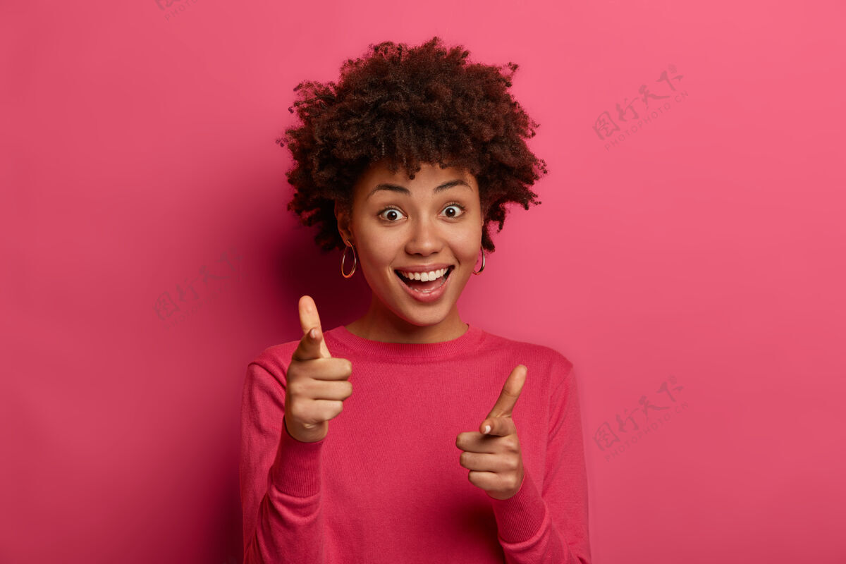 指标你被选中了高兴的 开朗的 友好的 看起来时髦的女孩有非洲发型 做手指枪的手势 愉快地在镜头前表示情绪食指手指