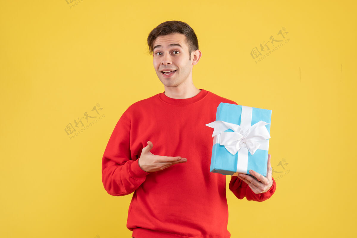 年轻人前视图穿着红色毛衣的年轻人在黄色背景上展示他的礼物快乐黄色休闲