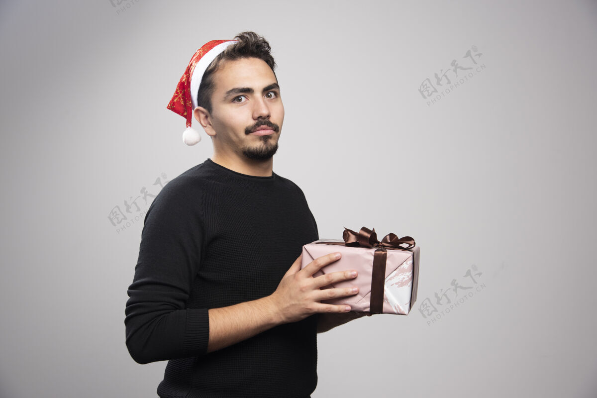 男孩一个戴着圣诞老人帽子拿着新年礼物的年轻人毛衣礼物男人