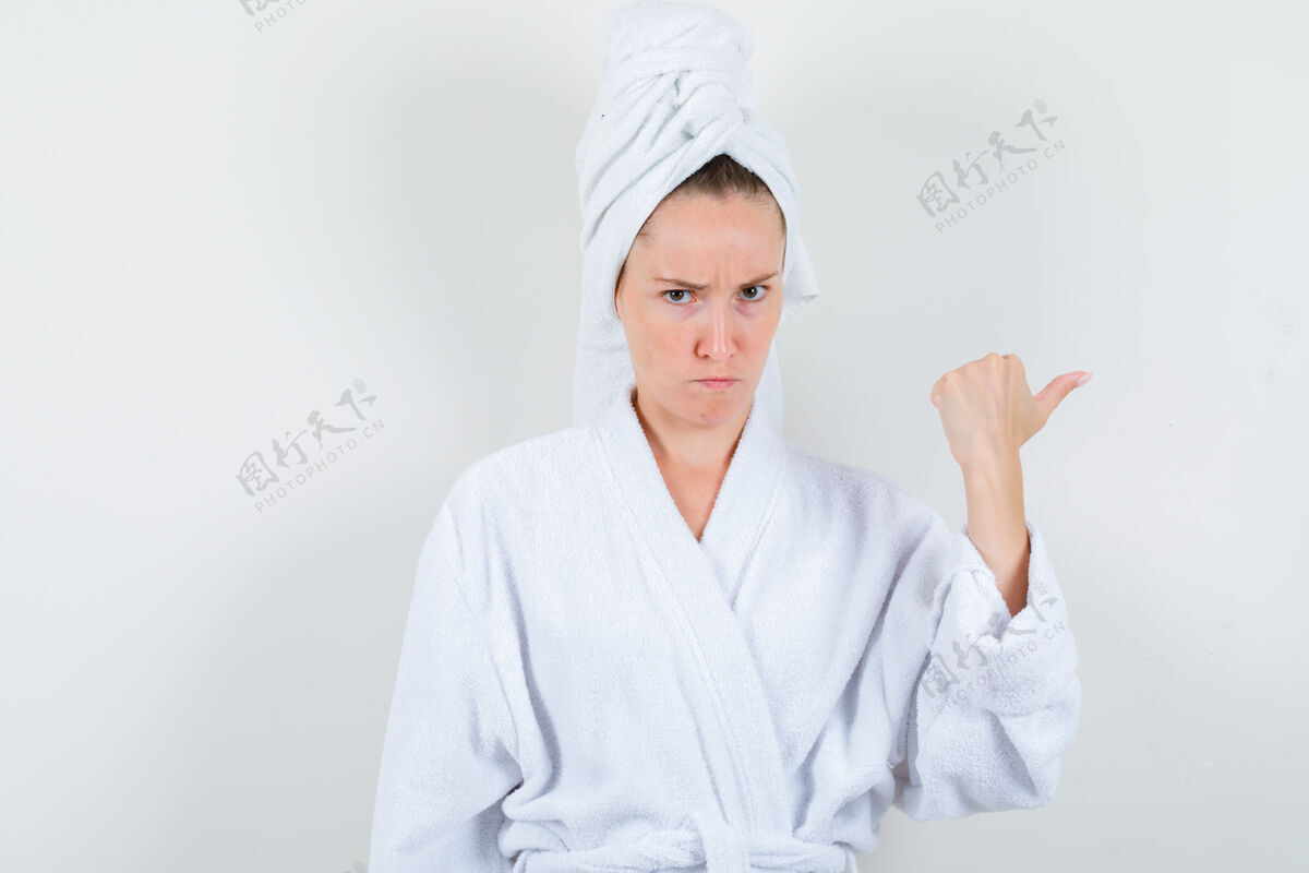 前面身穿白色浴袍的年轻女子 毛巾用拇指指向一边 神情可疑 正前方视图欢呼拇指优雅