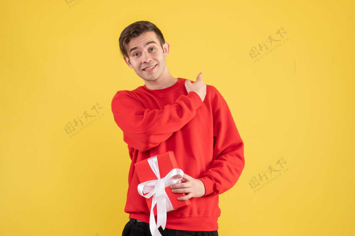 视图正面图：穿着红色毛衣的年轻人指着黄色背景的背面男性快乐毛衣