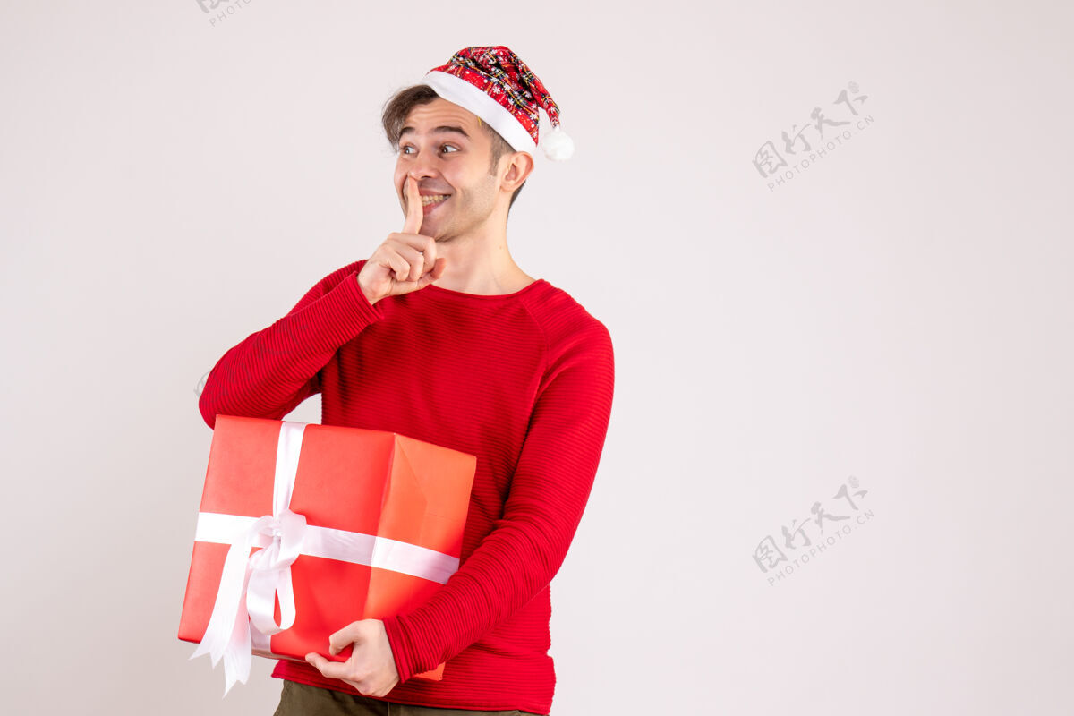 圣诞节前视图：戴着圣诞帽的年轻人在白色背景上做嘘标志微笑前面圣诞老人