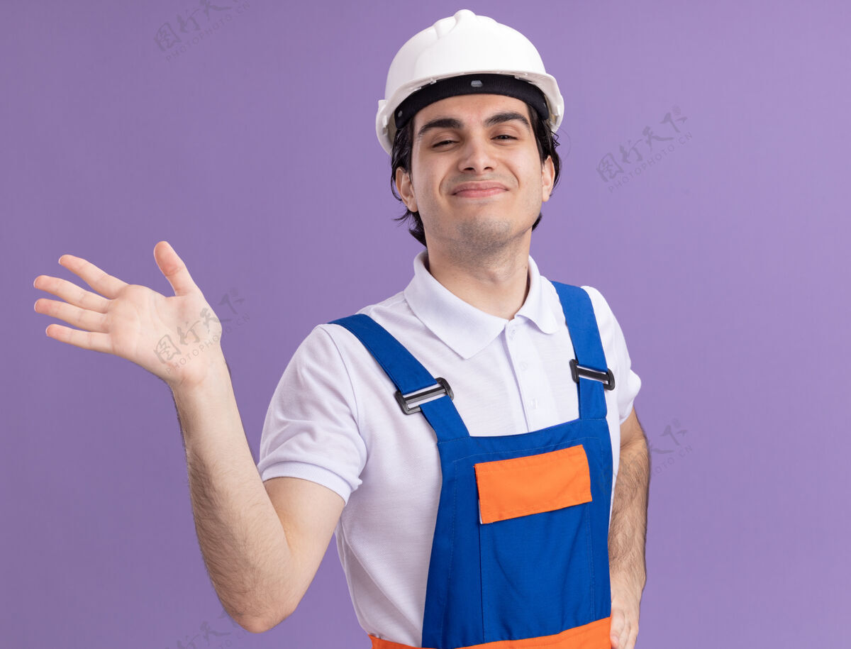 安全身穿施工制服 头戴安全帽的年轻建筑工人站在紫色的墙上 脸上挂着幸福的表情站立头盔男人