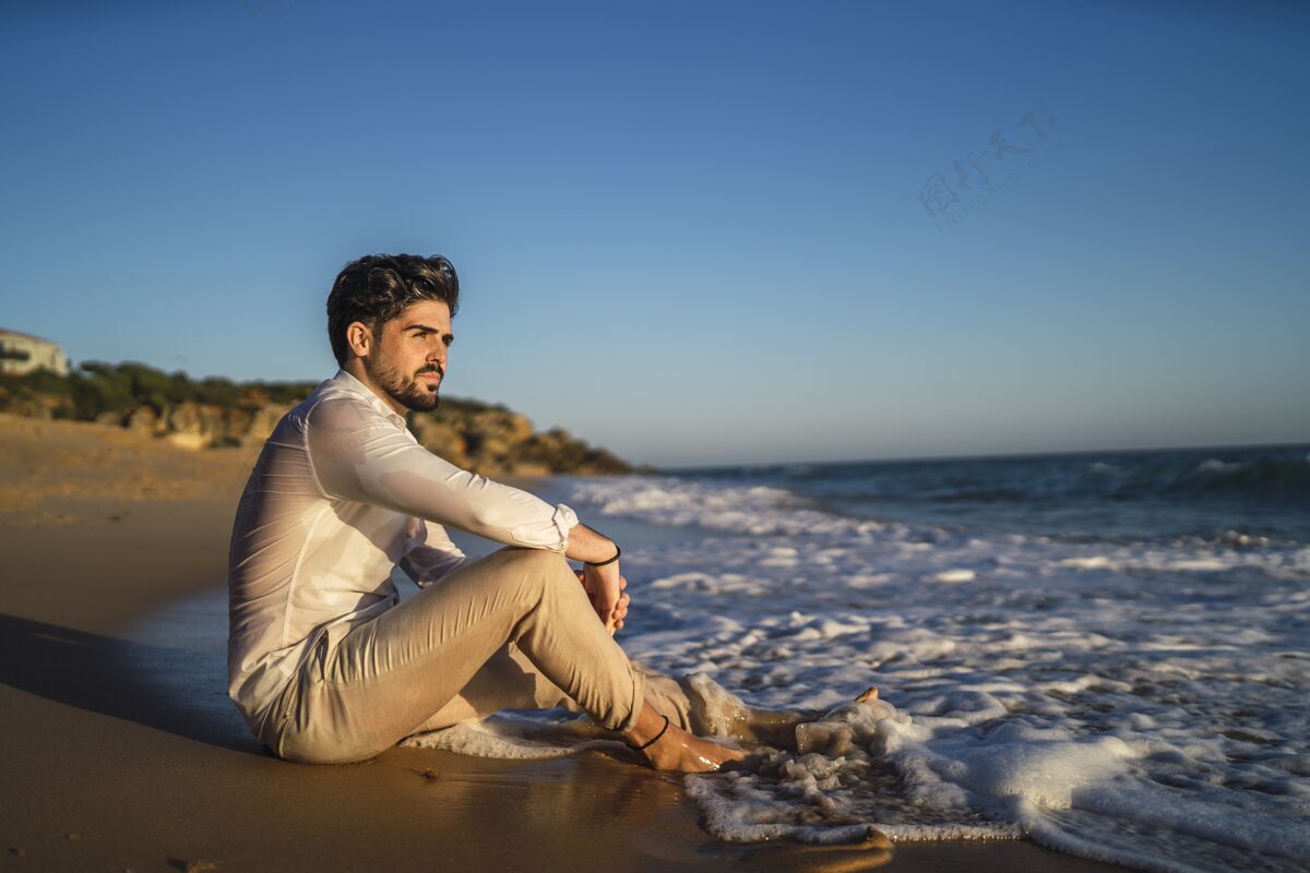 石头一个黑发男人坐在沙滩上的照片衬衫美丽地平线