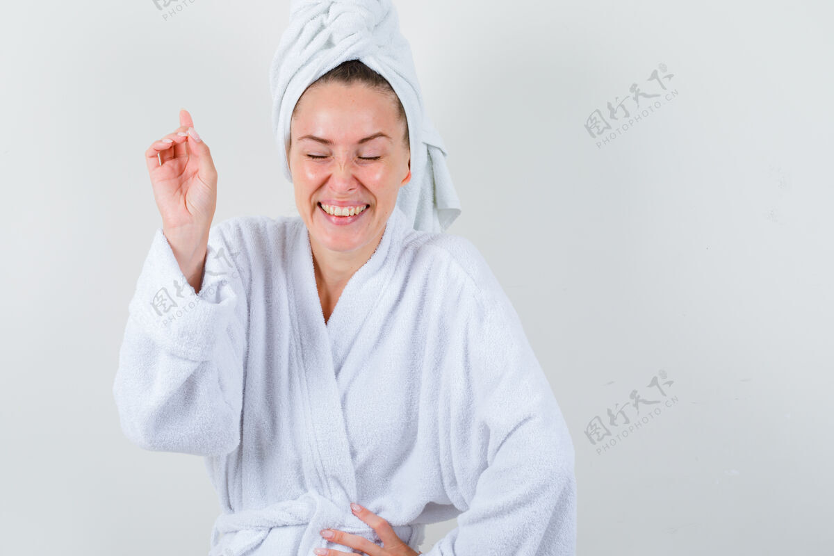 完美年轻的女士指着一边牵着手放在腰上 穿着白色浴衣 毛巾 看上去很开心 前视图护理亚洲人持有