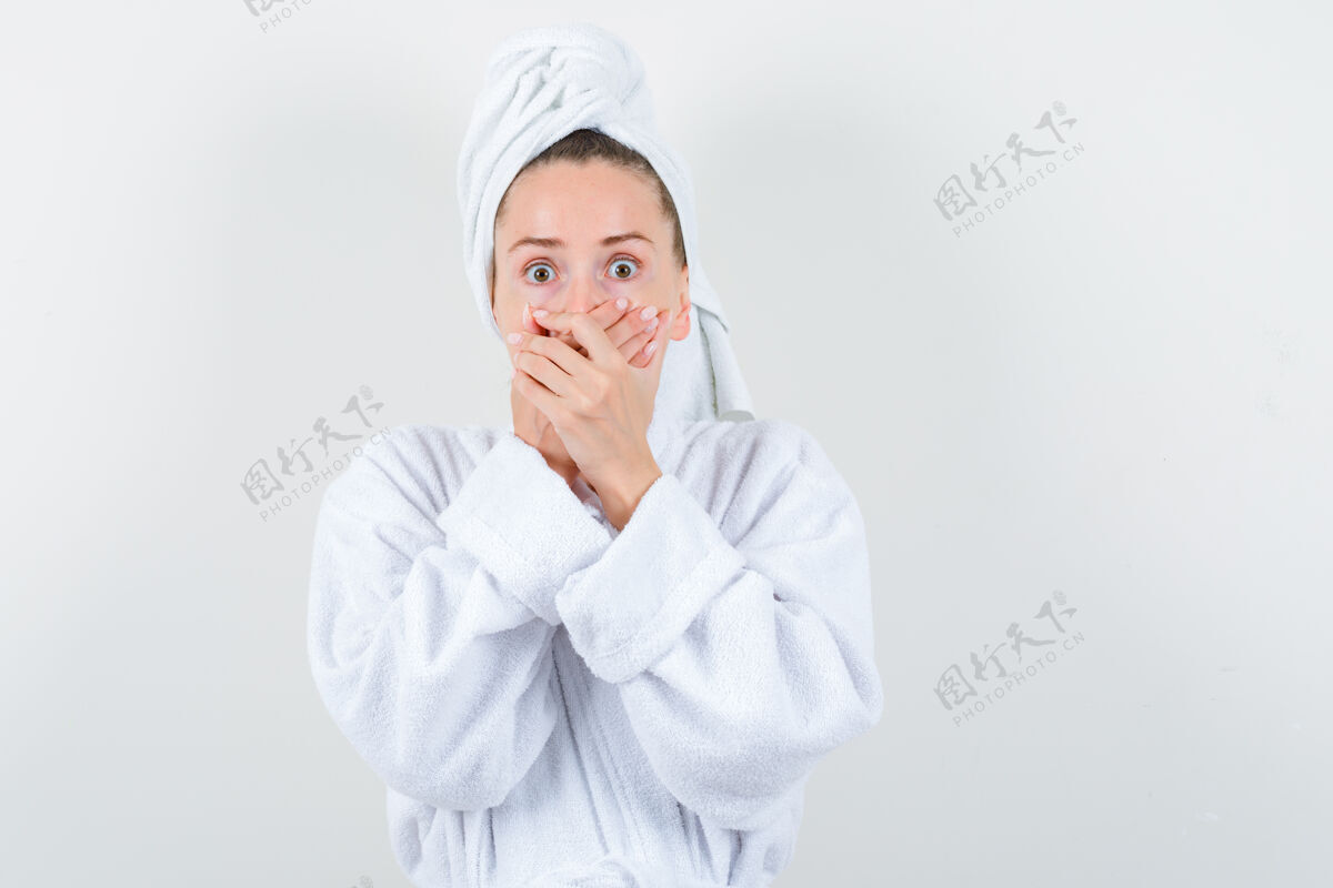 成人年轻的女孩手放在嘴上 穿着白色浴衣 脸上挂着毛巾 看上去很害怕 前视图害怕休闲年轻